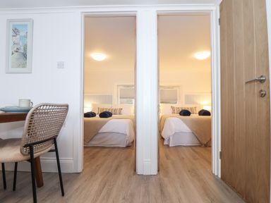 View of two bedrooms with beds seen through doorways and a dining table with chair in foreground at Harbour Studio in Sennen Cove