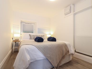 A bedroom with a double bed with white bedding blue towels and lamps on bedside tables at Harbour Studio in Sennen Cove