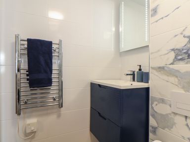 A bathroom with a blue towel on a chrome towel rack and a blue vanity unit with a sink and soap dispenser at Harbour Studio in Sennen Cove