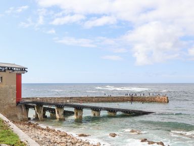 A coastal scene with a stone pier and a ramp leading to the sea with people on the pier at Harbour Studio in Sennen Cove