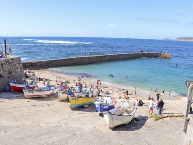 A small beach area with several boats on a ramp and people swimming and walking near a sea wall at Harbour Studio in Sennen Cove