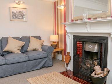 A living room with a gray sofa with beige cushions a side table with a lamp and a fireplace with firewood at Westholme Lodge in Minehead