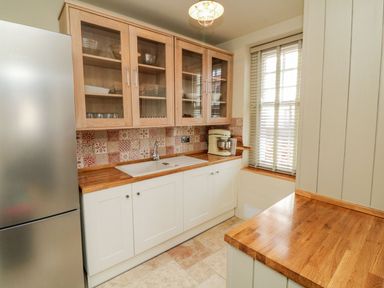 A kitchen with wooden countertops white cabinets a sink a stainless steel fridge and a window with blinds at Westholme Lodge in Minehead
