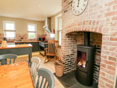 A kitchen with a wood burning stove in a brick fireplace and wooden chairs at Westholme Lodge in Minehead