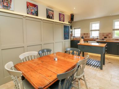 A kitchen with a wooden dining table and chairs a kitchen island and paintings on the wall at Westholme Lodge Minehead