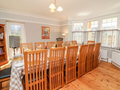 A dining room with a long table set for a meal with wooden chairs and a checkered tablecloth at Westholme Lodge in Minehead
