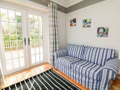 A room with a striped sofa three comic character pictures on the wall a glass door leading outside and a striped rug on a wooden floor at Westholme Lodge in Minehead