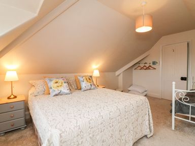 A bedroom with a double bed two bedside tables with lamps pillows on the bed a clothes rack with hangers a door and a ceiling light at Westholme Lodge in Minehead