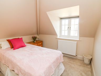 A bedroom with a bed covered in a pink blanket a wooden dresser with flowers and a window at Westholme Lodge in Minehead