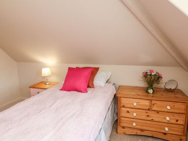 A bedroom with a bed between two wooden bedside tables one with a lamp the other with flowers and a mirror at Westholme Lodge in Minehead