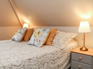 A bedroom with a bed covered in patterned bedding and pillows next to a nightstand with a lamp at Westholme Lodge in Minehead