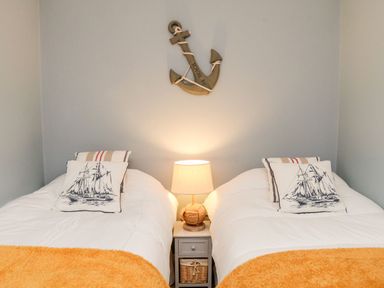 A bedroom with two single beds a wooden anchor wall decoration and a bedside table with a lamp at Westholme Lodge in Minehead