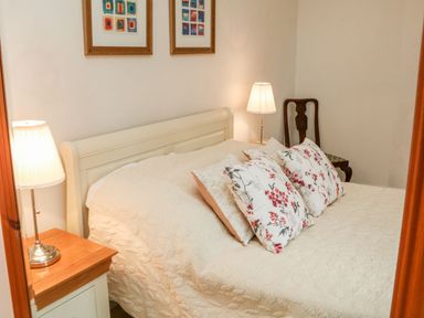 A bedroom with a bed with floral pillows two lamps on bedside tables and framed pictures on the wall at Westholme Lodge in Minehead