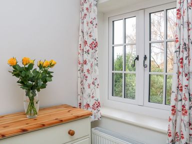 A vase with yellow roses on a wooden dresser near a window with floral curtains at Westholme Lodge Minehead