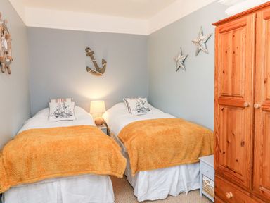 A bedroom with two single beds with orange blankets and a wooden wardrobe at Westholme Lodge in Minehead