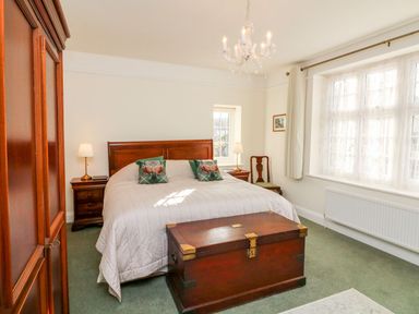 A bedroom with a bed pillows a wooden chest bedside tables lamps a chair and a window at Westholme Lodge in Minehead