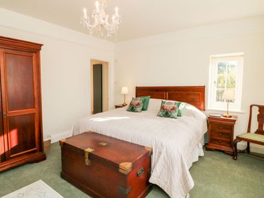 A bedroom with a large bed two bedside tables a wooden chest a wardrobe and a chair at Westholme Lodge in Minehead