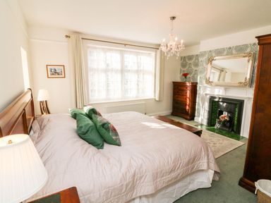 A bedroom with a bed green pillows a fireplace with a mirror above a chest of drawers and a chandelier at Westholme Lodge Minehead