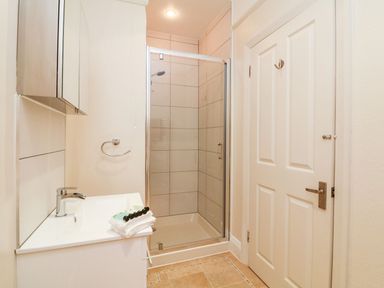 A bathroom with a white sink cabinet and towels next to a glass shower enclosure and a closed white door at Westholme Lodge in Minehead