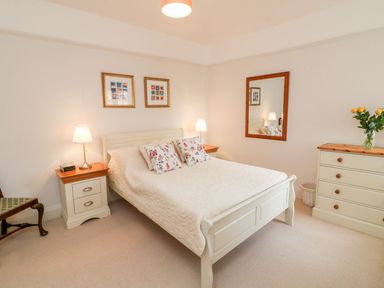 A bedroom with a double bed flanked by two bedside tables with lamps a dresser with flowers in a vase a mirror and framed pictures on the wall at Westholme Lodge in Minehead