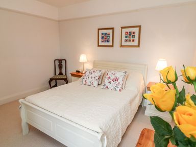 A bedroom with a white bed and floral pillows two bedside tables with lamps and a chair at Westholme Lodge in Minehead