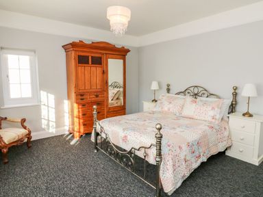A bedroom with a metal bed frame with floral bedding two bedside tables with lamps a wooden wardrobe and a wooden chair at Westholme Lodge in Minehead