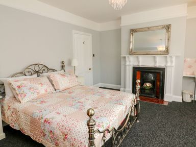 A bedroom with a metal bed frame and floral quilt a white fireplace with a mirror above at Westholme Lodge in Minehead