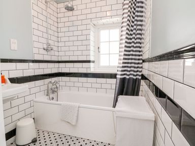 A bathroom with a bathtub showerhead striped shower curtain and a window at Westholme Lodge in Minehead