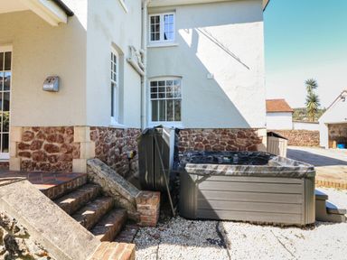An outdoor area with a hot tub next to a house with brick steps and gravel ground at Westholme Lodge in Minehead