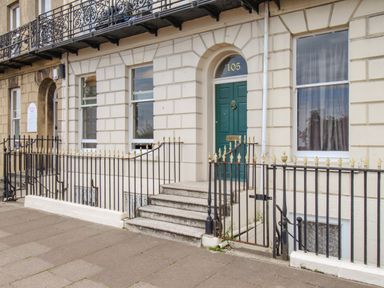 The front entrance of a beige stone building with a green door numbered 105 and black iron railings outside at Sunbeach in Weymouth