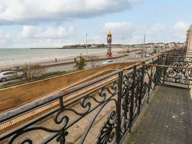 A balcony with decorative railings overlooking a road beach a clock tower and the sea at Sunbeach in Weymouth
