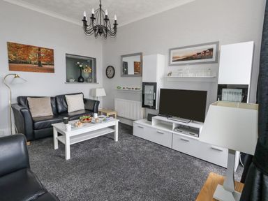 A living room with black leather sofas white coffee table with cups and food and a white TV cabinet with a television at Sunbeach Weymouth