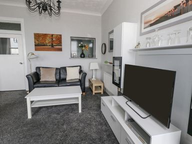 A living room with a black sofa two cushions a white coffee table and a television on a white stand at Sunbeach Weymouth