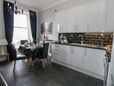 A kitchen with a dining table set with dishes and wine near a window with black curtains at Sunbeach in Weymouth
