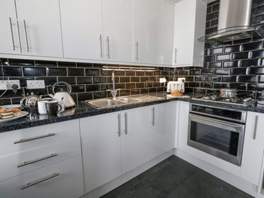 A kitchen with white cabinets black tiled backsplash a sink oven stove kettle and toaster at Sunbeach in Weymouth