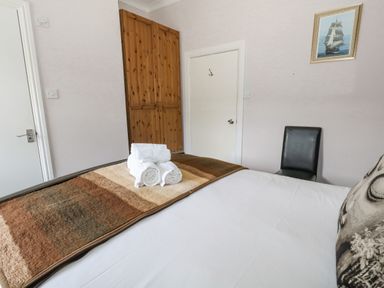 A bedroom with a bed with folded towels and a blanket a wooden wardrobe a black chair a framed picture on the wall at Sunbeach in Weymouth