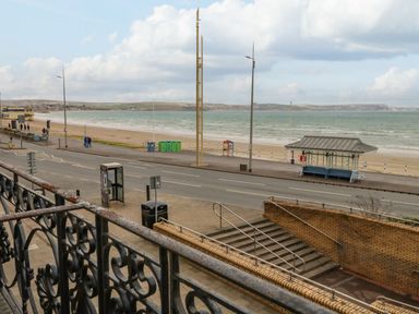 A view of a beach with a sandy shore a road with a bus shelter and a phone booth from a balcony at Sunbeach in Weymouth