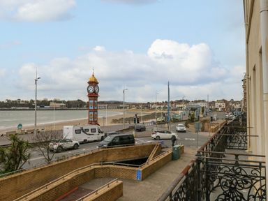 A street view with a clock tower near a beach and parked vehicles at Sunbeach in Weymouth