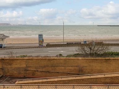A view of a beach with a road and a brick wall in the foreground at Sunbeach Weymouth