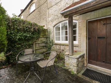 An outdoor patio with a round glass table and two chairs next to a stone wall and wooden door at Field Cottage in Shepton Mallet