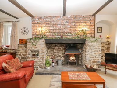 A living room with a stone fireplace red sofa wooden coffee table and a television at Field Cottage in Shepton Mallet