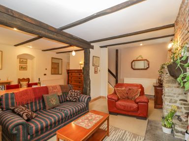 A living room with striped sofa and red armchair near stone fireplace at Field Cottage in Shepton Mallet