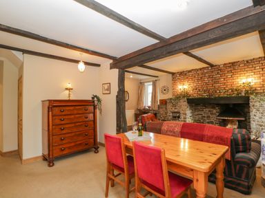 A dining area with a wooden table and red chairs next to a stone fireplace and a wooden chest of drawers at Field Cottage in Shepton Mallet