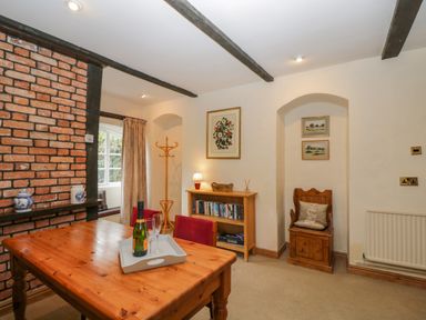 A dining room with wooden table and chairs a bookcase and a coat rack at Field Cottage in Shepton Mallet