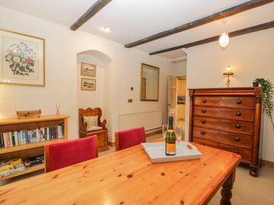 A dining room with a wooden table and red chairs a wooden dresser bookshelf and wall art at Field Cottage in Shepton Mallet