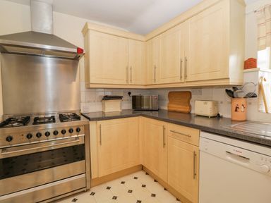 A kitchen with wooden cabinets a stainless steel stove a microwave toaster and dishwasher at Field Cottage in Shepton Mallet