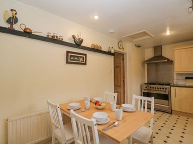 A kitchen with a wooden dining table set for four and a stainless steel stove at Field Cottage in Shepton Mallet