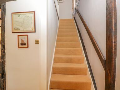 A staircase with beige carpet tilting upward with two framed pictures on a white wall at Field Cottage in Shepton Mallet