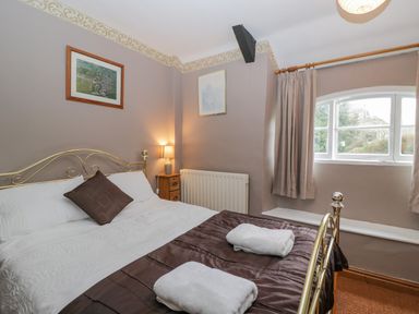 A bedroom with a metal bed frame bedside table with a lamp framed pictures and curtains at Field Cottage in Shepton Mallet