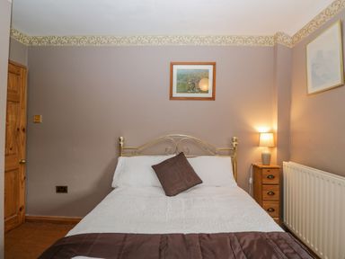 A bedroom with a double bed a wooden door a bedside table with a lamp and framed pictures on the wall at Field Cottage in Shepton Mallet